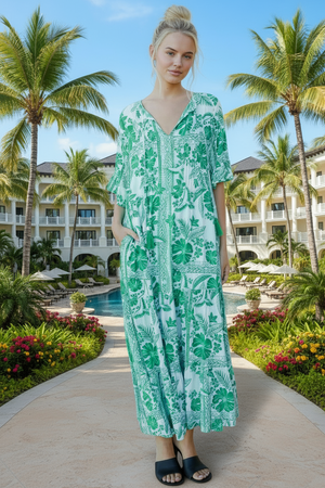 Woman in a green floral dress standing in a tropical resort setting with palm trees and a pool.