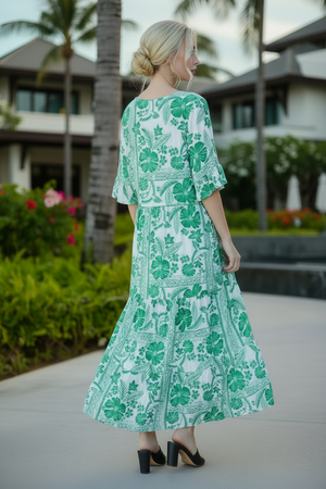 Woman in a green floral dress standing outdoors with palm trees and a building in the background