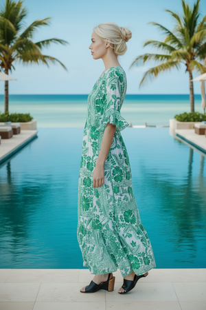 Woman in a green floral dress standing by a pool with palm trees in the background
