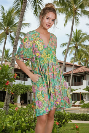 Woman wearing a colorful patterned dress in a tropical setting with palm trees and a building.