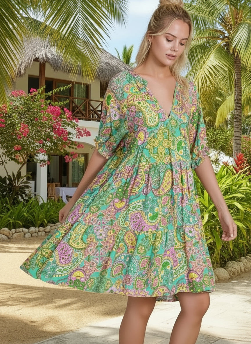 Woman wearing a colorful patterned dress in a tropical setting with palm trees and a building.