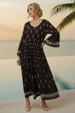 Woman in a black patterned dress standing on a beach with palm trees and ocean in the background