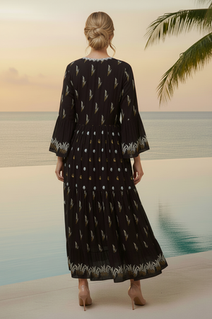 Woman wearing a black dress with white patterns standing on a beach.