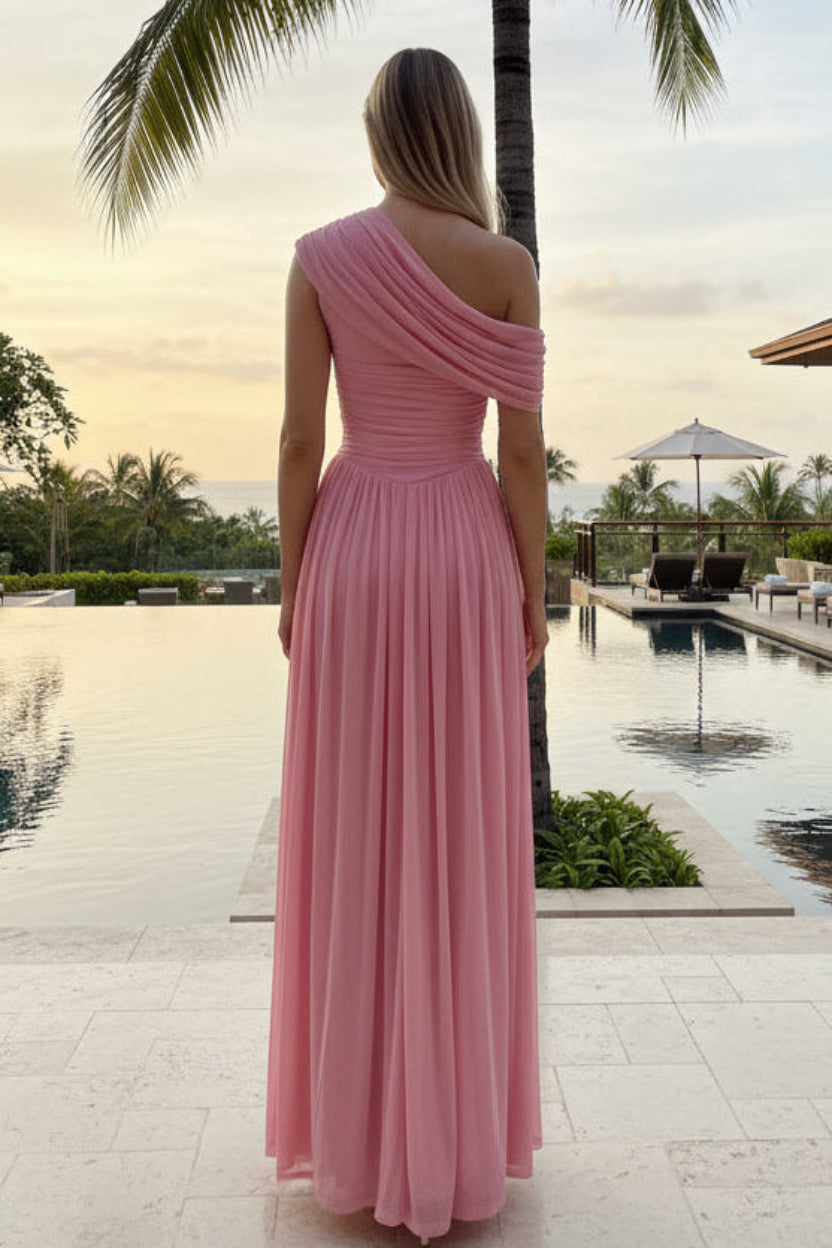 Woman in a pink one-shoulder dress standing by a poolside with palm trees in the background