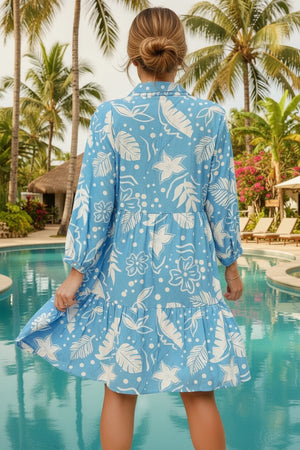 Woman wearing a blue floral dress by a pool with palm trees in the background