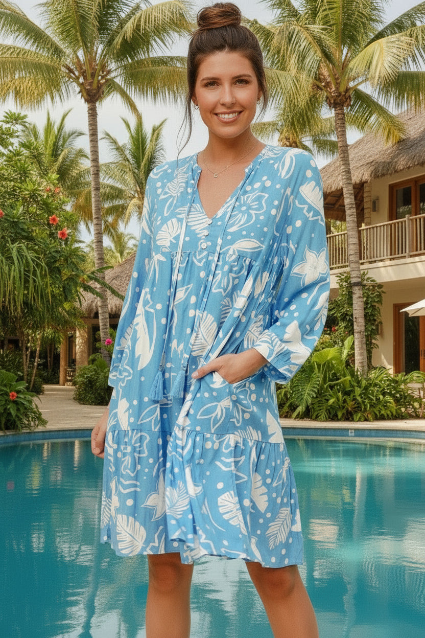 Woman in a blue floral dress standing by a pool with palm trees in the background