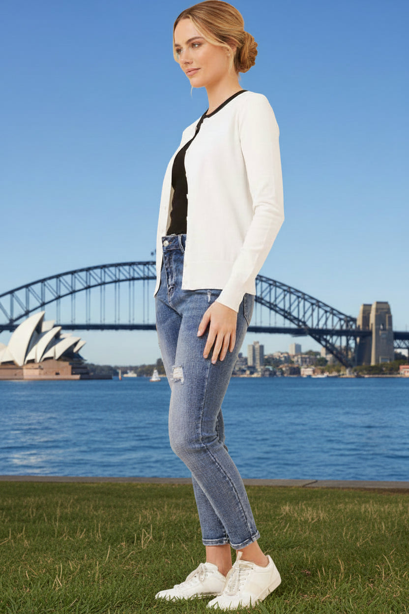 Woman wearing a white cardigan and blue jeans standing in front of the Sydney Harbour Bridge.