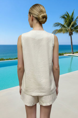 Woman in a beige outfit standing by a pool with ocean view