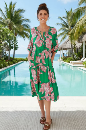 Woman in a green floral dress standing in a tropical-themed room with plants and furniture.