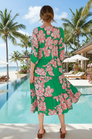 Woman in a green floral dress standing by a pool with palm trees in the background