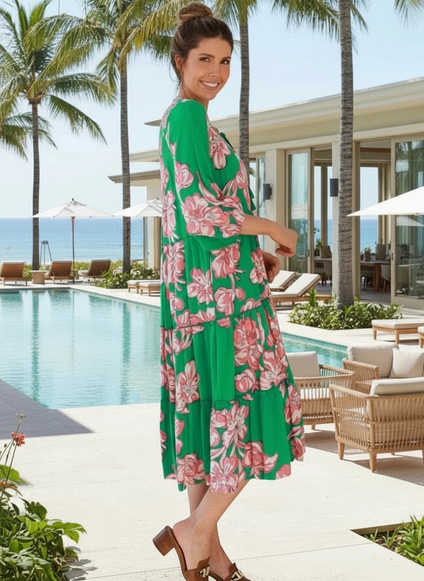 Woman in a green floral dress standing in a tropical-themed room with plants and furniture.