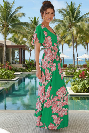 Woman in a green floral dress standing on a patio with a cactus and chair in the background.