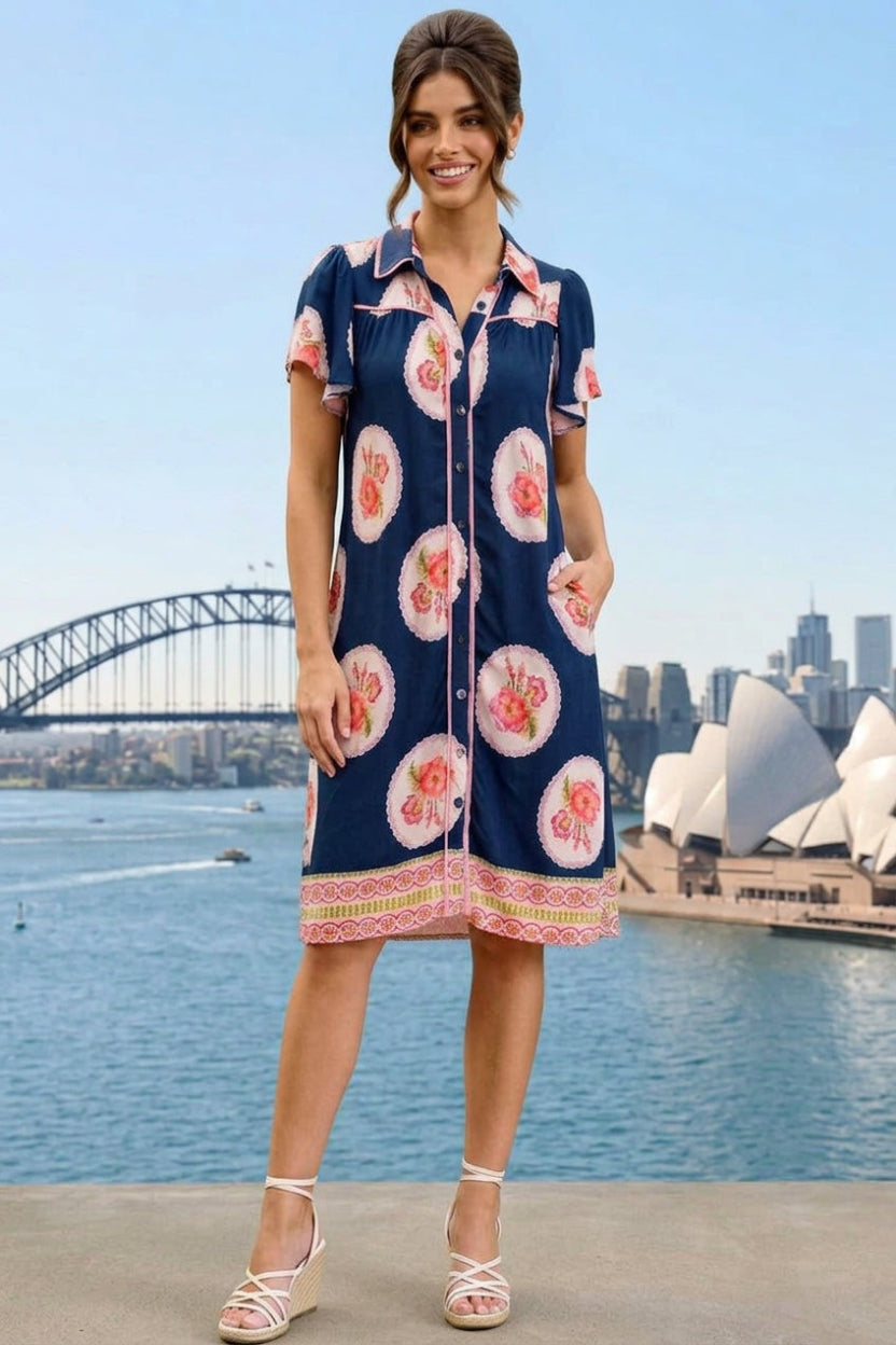 A woman wearing a navy blue short-sleeve button-up dress with a pink and white tropical floral print
