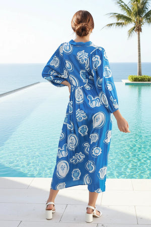 Woman wearing a blue patterned dress by a pool with palm trees in the background