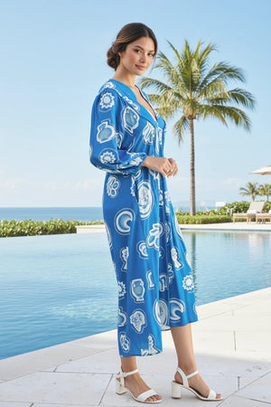 Woman in a blue patterned dress standing by a pool with palm trees in the background