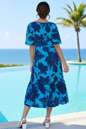Woman wearing a blue floral dress by a pool with palm trees and ocean view