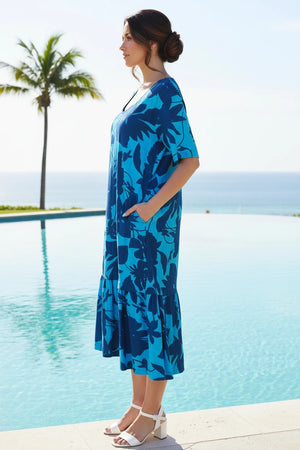Woman wearing a blue floral dress by a pool with palm trees in the background