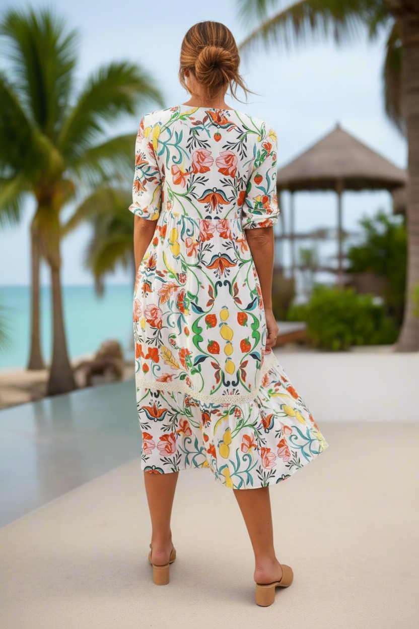 Woman in a floral dress standing by a pool with palm trees and a gazebo in the background.