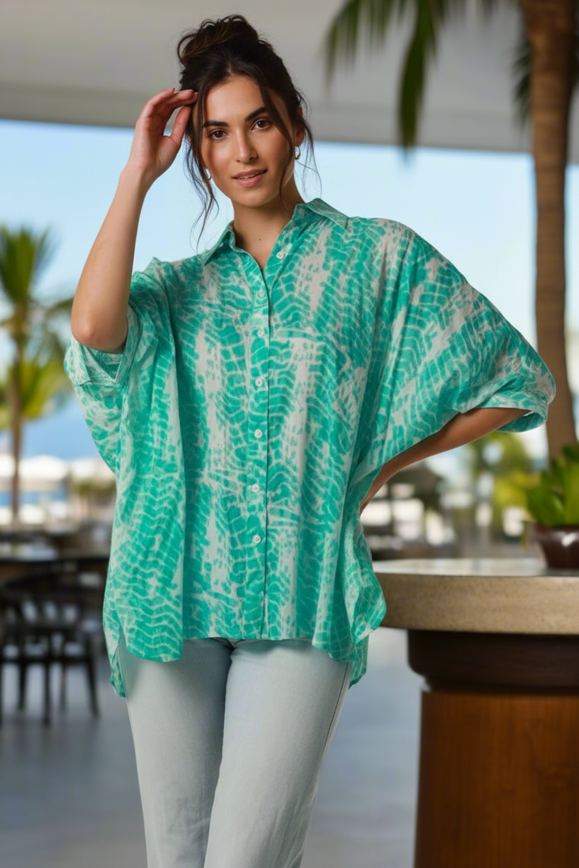 Woman wearing a green and white patterned top with a blurred outdoor background