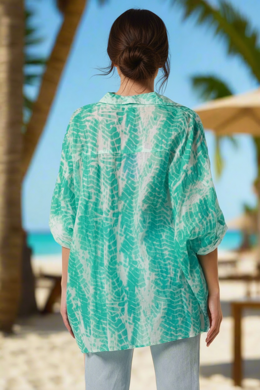 Woman wearing a green and white patterned shirt on a beach with palm trees in the background