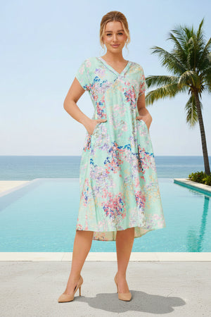 Woman in a floral dress standing by a pool with palm trees and ocean view