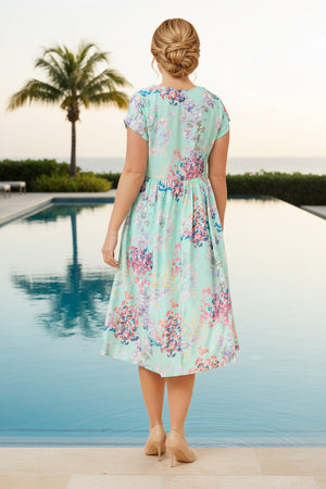 Woman in a floral dress standing by a pool with palm trees in the background