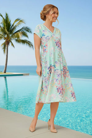 Woman in a floral dress standing by a pool with palm trees and blue sky in the background
