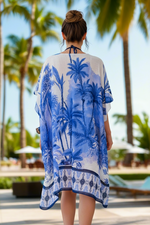 Woman wearing a blue palm tree patterned cover-up in a tropical setting.
