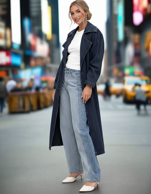 Woman wearing a long dark coat, white shirt, and light blue jeans in an urban setting.