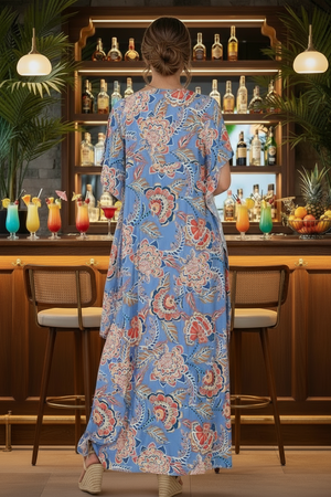Woman in a blue floral dress standing in front of a bar with drinks and bottles.