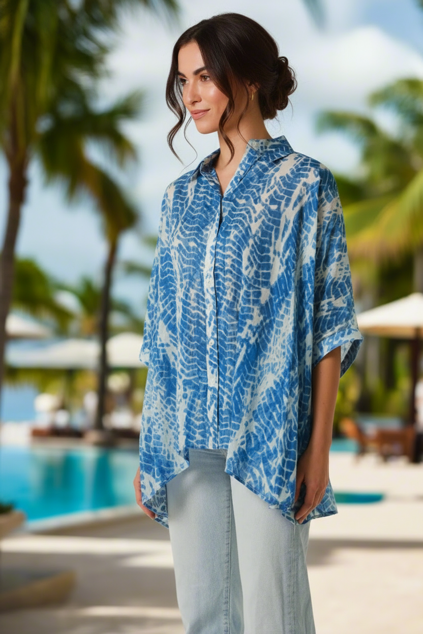 Woman wearing a blue and white patterned shirt by a poolside with palm trees in the background