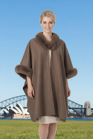 Woman wearing a brown poncho with faux  fur trim standing in front of the Sydney Opera House and Harbour Bridge.