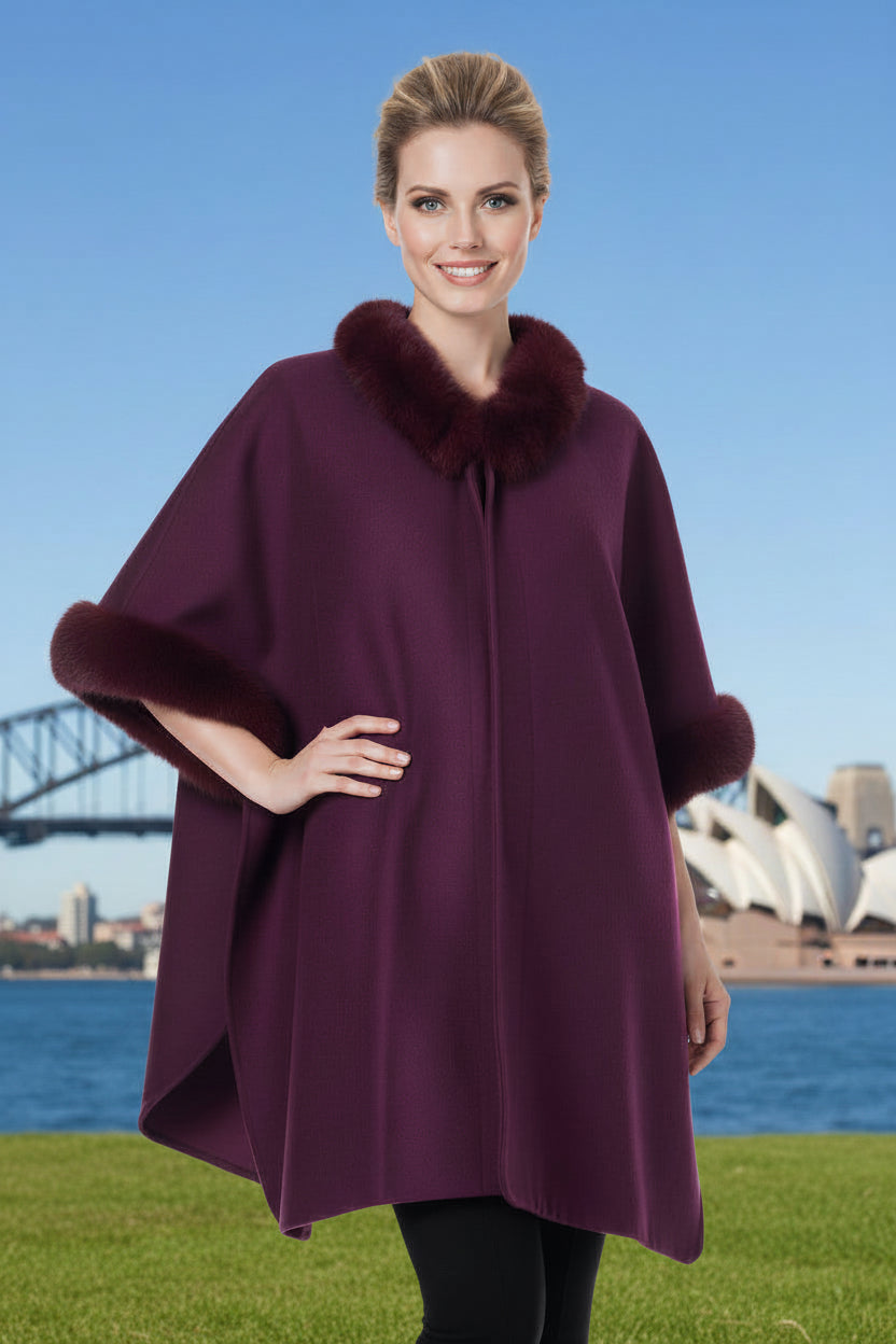 Woman wearing a burgandy poncho with faux fur trim in front of the Sydney Opera House.