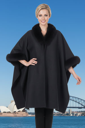 Woman wearing a deep forest green faux fur-trimmed poncho with the Sydney Opera House and Harbour Bridge in the background.