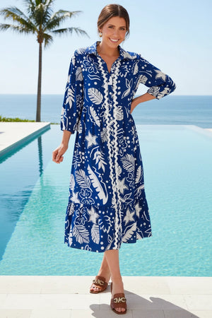 Woman wearing a blue and white patterned dress by a pool with palm trees and ocean in the background