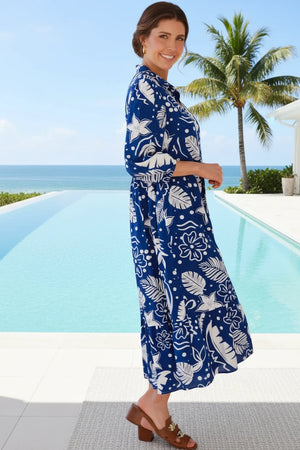 Woman wearing a blue floral dress by a pool with palm trees in the background