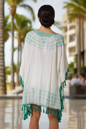 Woman wearing a white and green dress with fringes in a tropical setting.