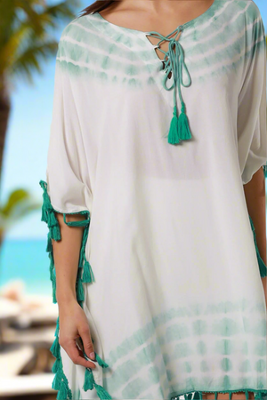White dress with green accents and tassels on a beach background