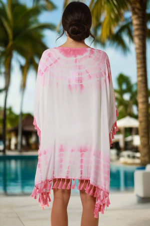 Person wearing a pink and white tie-dye cover-up with palm trees and a pool in the background