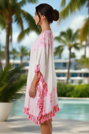 Woman wearing a white and pink dress with ruffled details by a poolside with palm trees in the background.