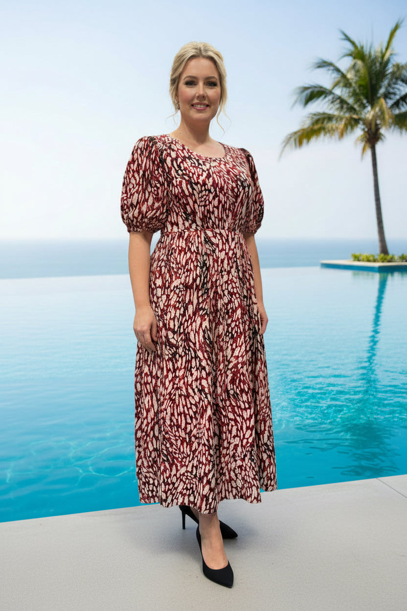 Woman in a patterned dress standing by a pool with palm trees in the background