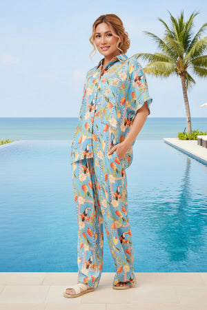 Woman in a floral outfit standing by a pool with palm trees in the background