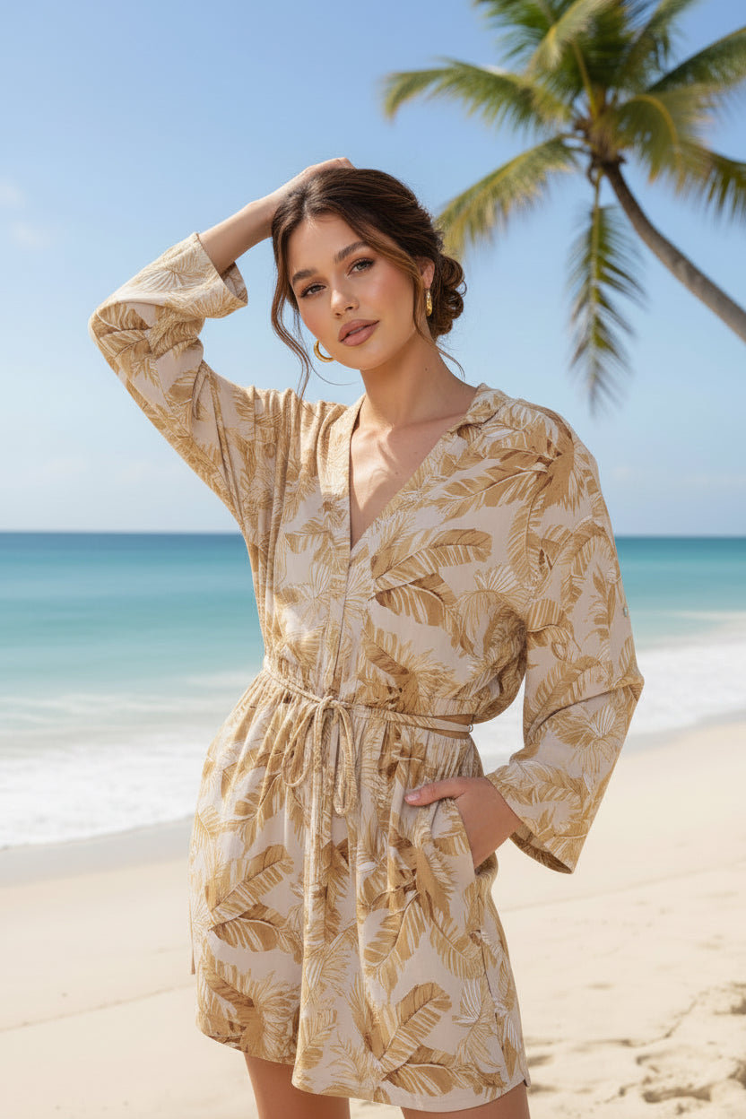 Woman in a beige floral dress standing on a beach with palm trees in the background