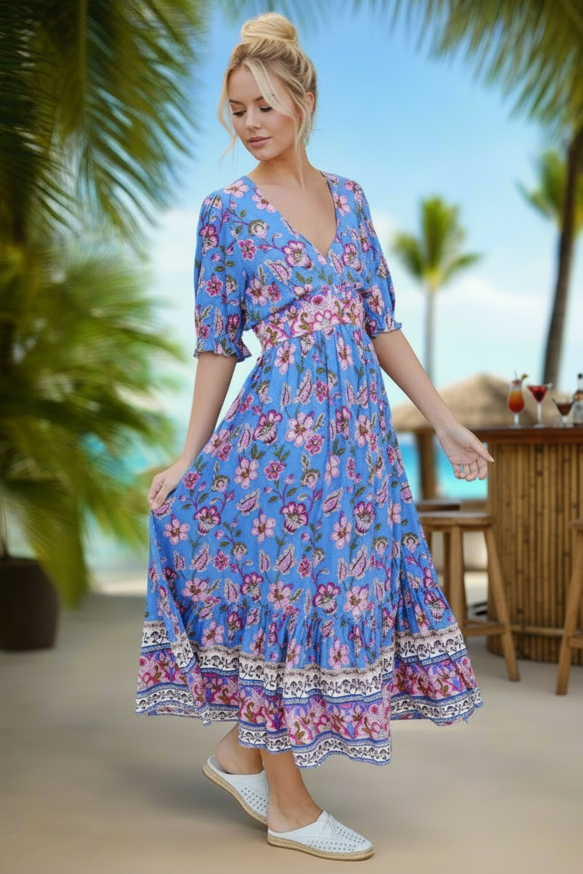 Woman in a blue floral dress standing in a tropical setting with palm trees and a bar.