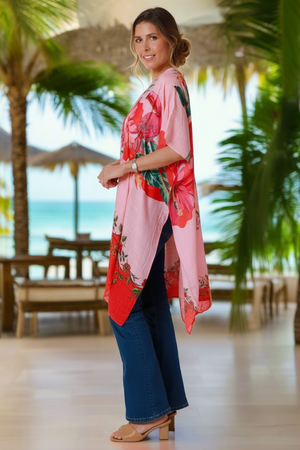 Woman wearing a pink floral kimono in a tropical setting with palm trees and ocean view.