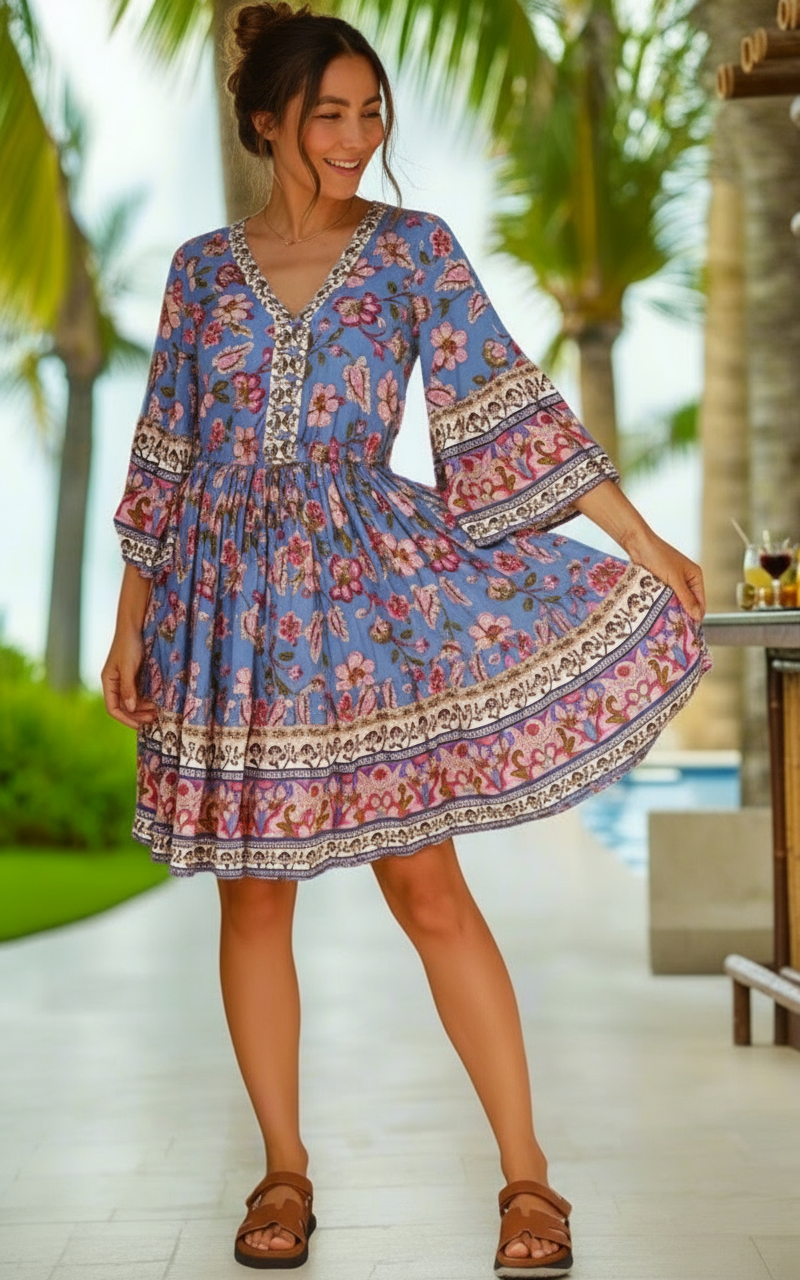 Woman in a blue floral dress standing by a poolside with palm trees in the background