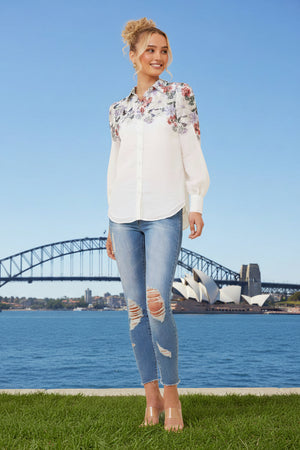 Woman wearing a white floral blouse and ripped jeans 