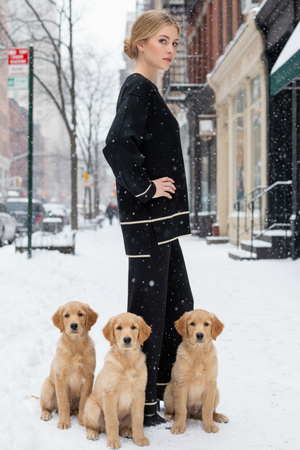 Woman in black outfit standing with three golden retriever puppies on a snowy street.