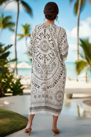 Woman wearing a black and white patterned dress standing by a pool with palm trees in the background