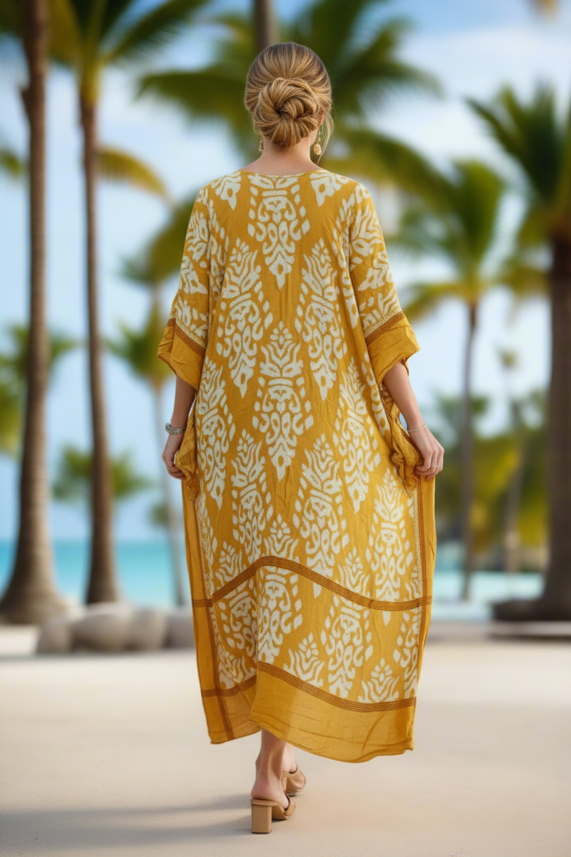 Woman in a yellow dress with white patterns walking on a beach with palm trees in the background